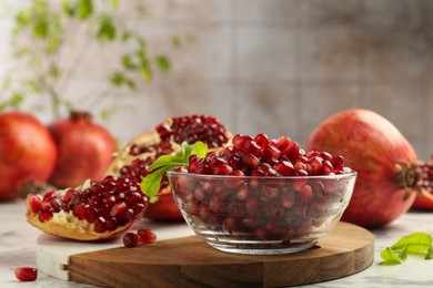Photo of Ripe juicy pomegranate grains in bowl and green leaves on white table