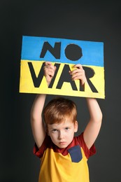 Photo of Boy holding poster in colors of Ukrainian national flag with phrase No War against grey background