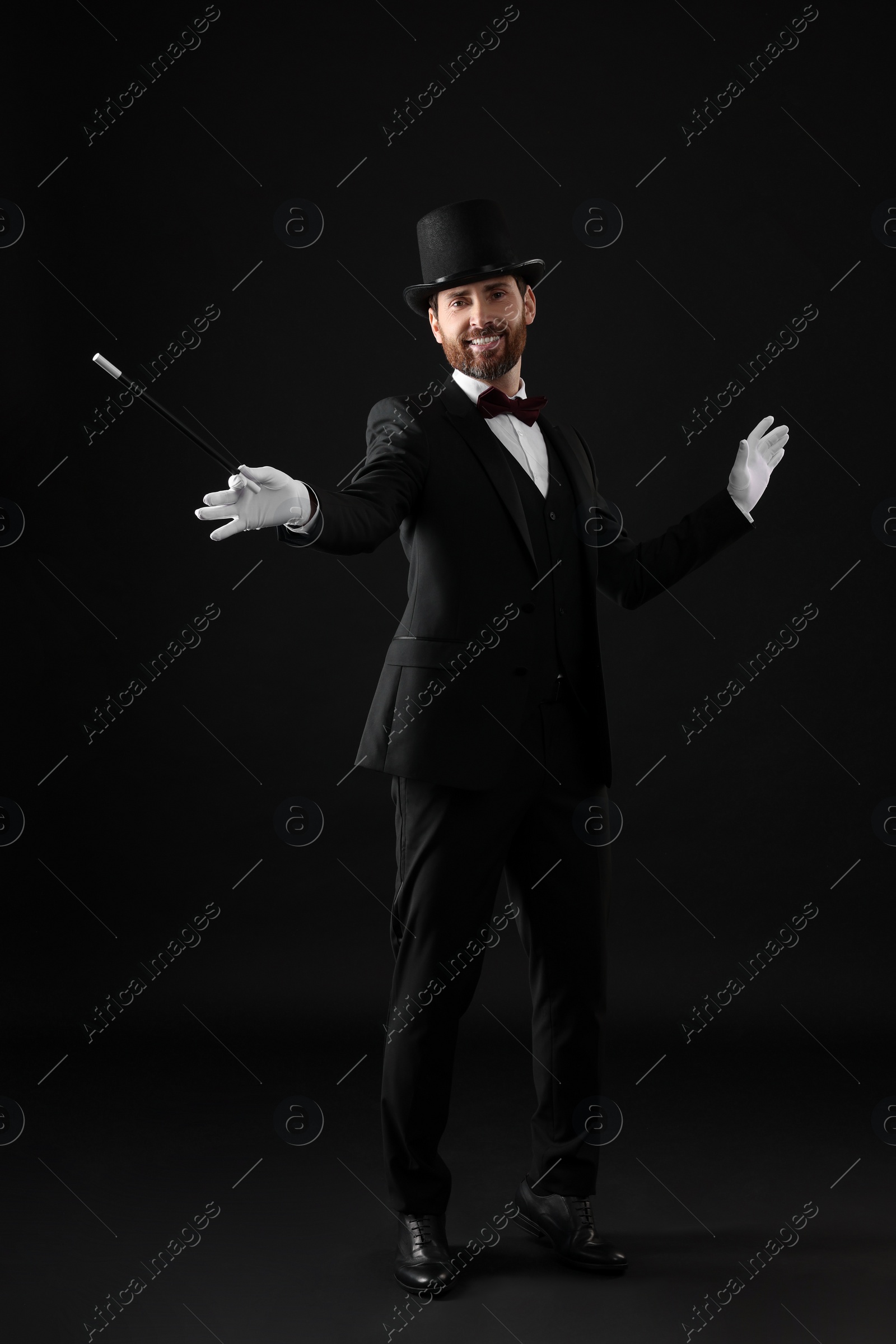 Photo of Happy magician in top hat holding wand on black background