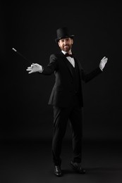 Photo of Happy magician in top hat holding wand on black background