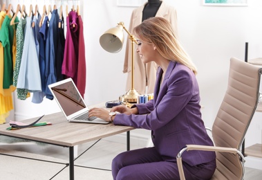 Beautiful young stylist working with laptop in studio. Trendy clothes