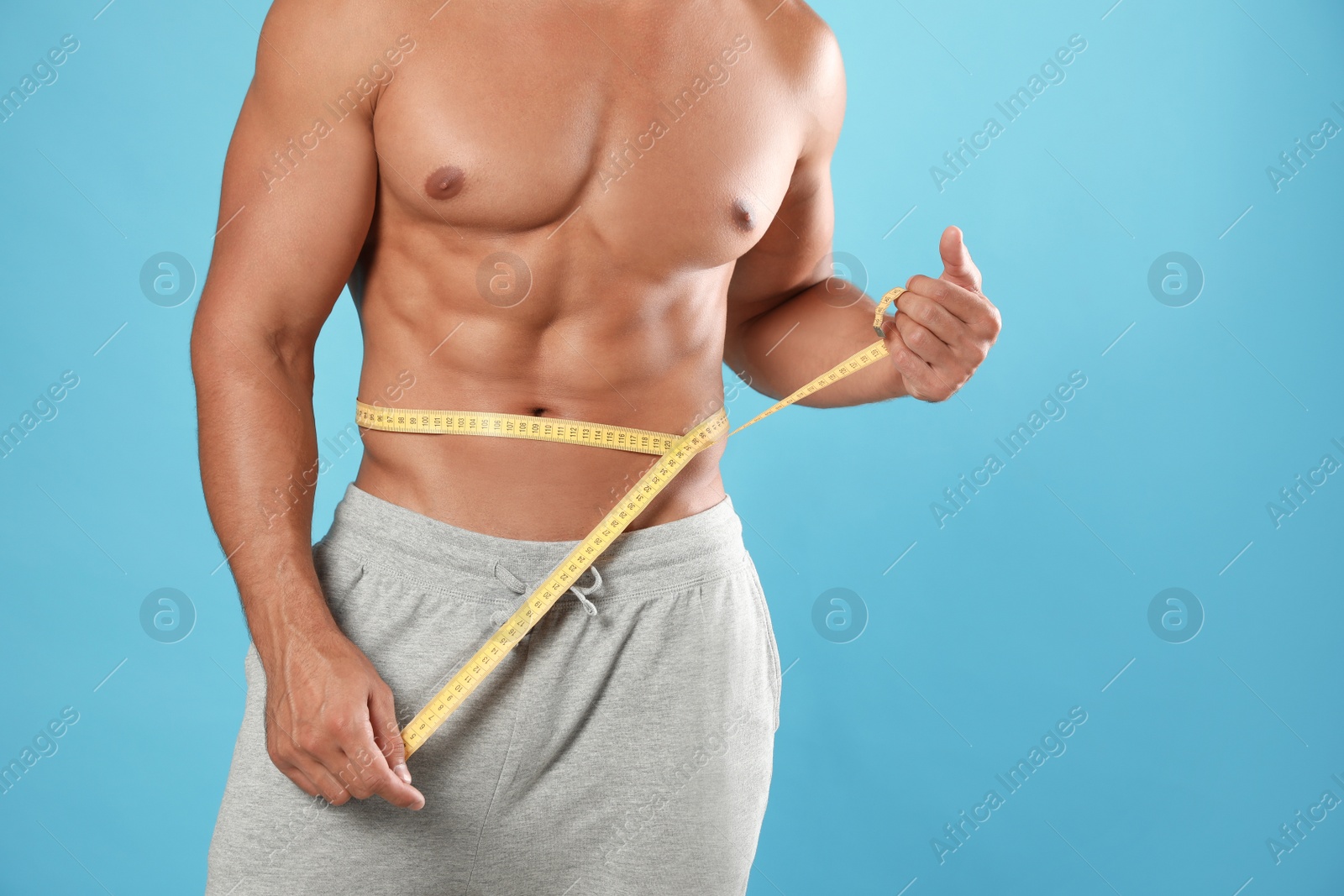 Photo of Young man with slim body using measuring tape on light blue background, closeup view. Space for text