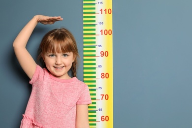 Photo of Little girl measuring her height on color background