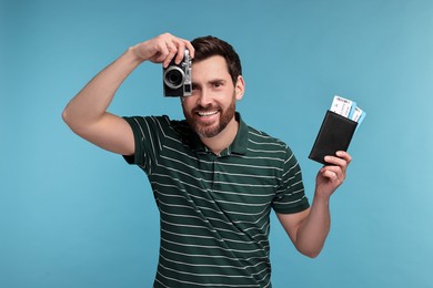 Smiling man with passport, camera and tickets on light blue background