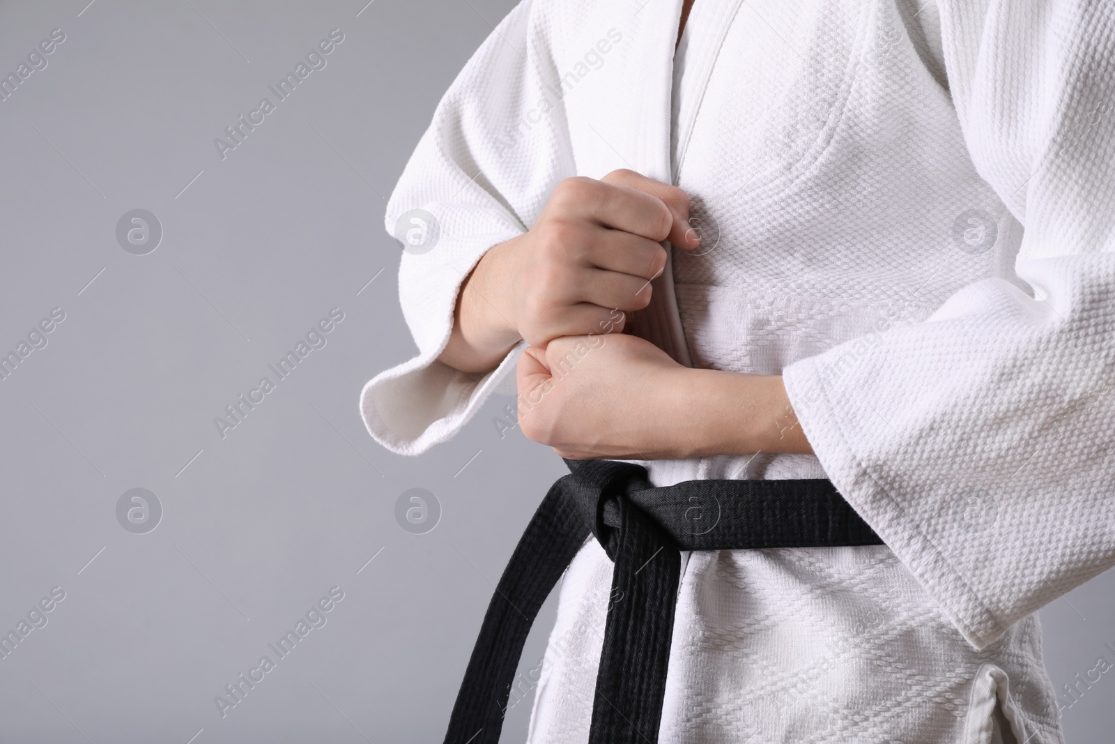 Photo of Martial arts master in keikogi with black belt on grey background, closeup