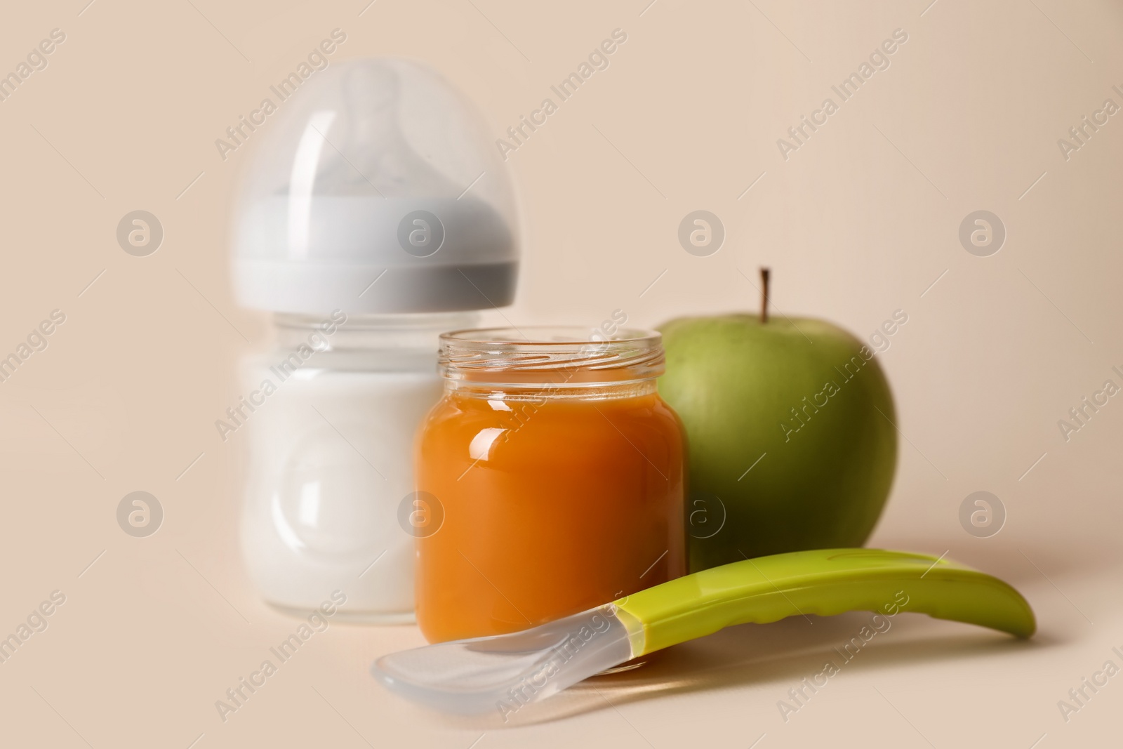 Photo of Healthy baby food in jar, bottle of milk, apple and spoon on beige background