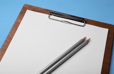 Photo of Clipboard with sheet of paper and pencils on light blue wooden table, closeup