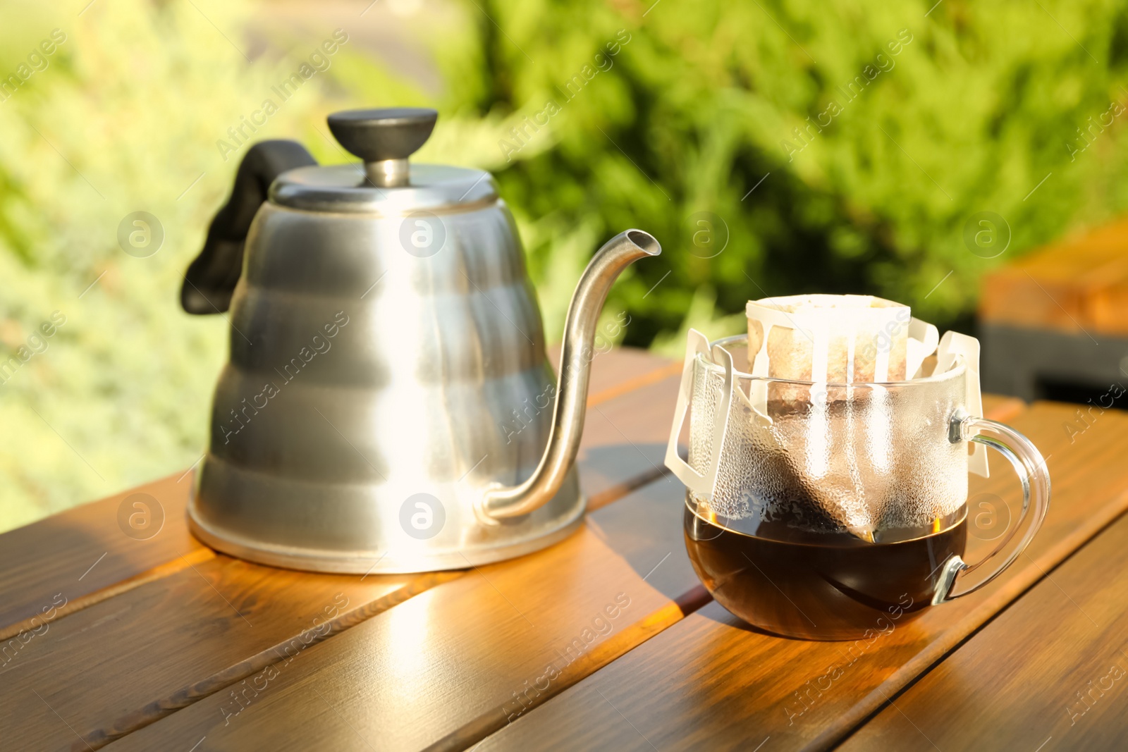 Photo of Glass cup with drip coffee bag and kettle on wooden table