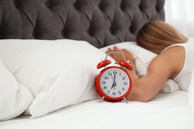 Photo of Analog alarm clock and sleepy woman in bed. Time of day