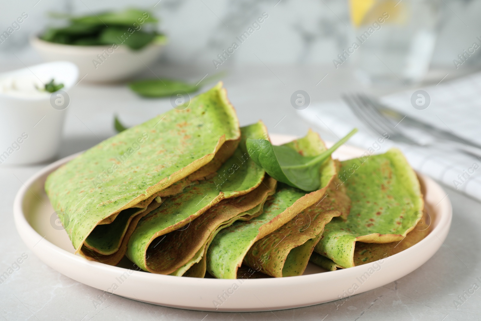 Photo of Tasty spinach crepes on light grey table, closeup