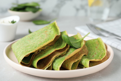 Tasty spinach crepes on light grey table, closeup