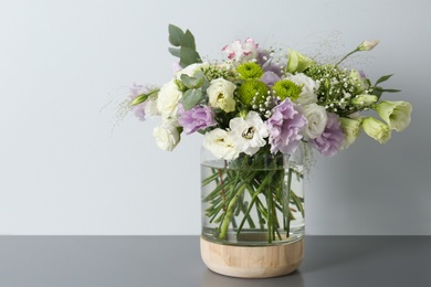 Photo of Bouquet with beautiful Eustoma flowers in vase on grey table against light background