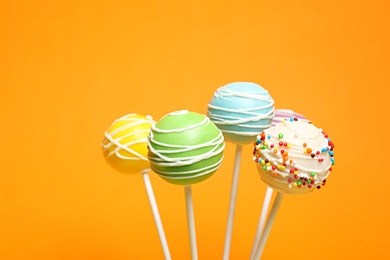 Many bright delicious cake pops on color background