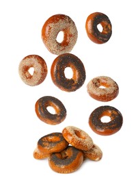 Many fresh bagels with poppy and sesame seeds falling into pile on white background