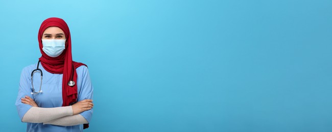 Image of Muslim woman in hijab, medical uniform and protective mask on light blue background, space for text. Banner design