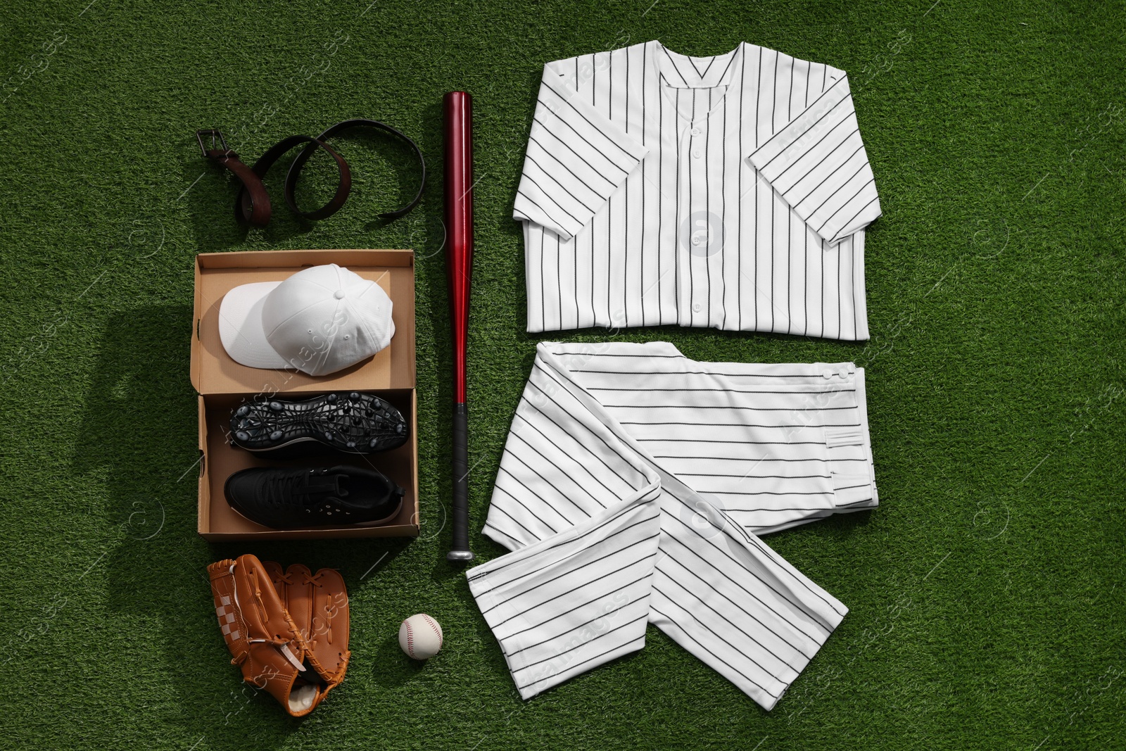 Photo of Baseball uniform and other sports equipment on artificial grass, flat lay