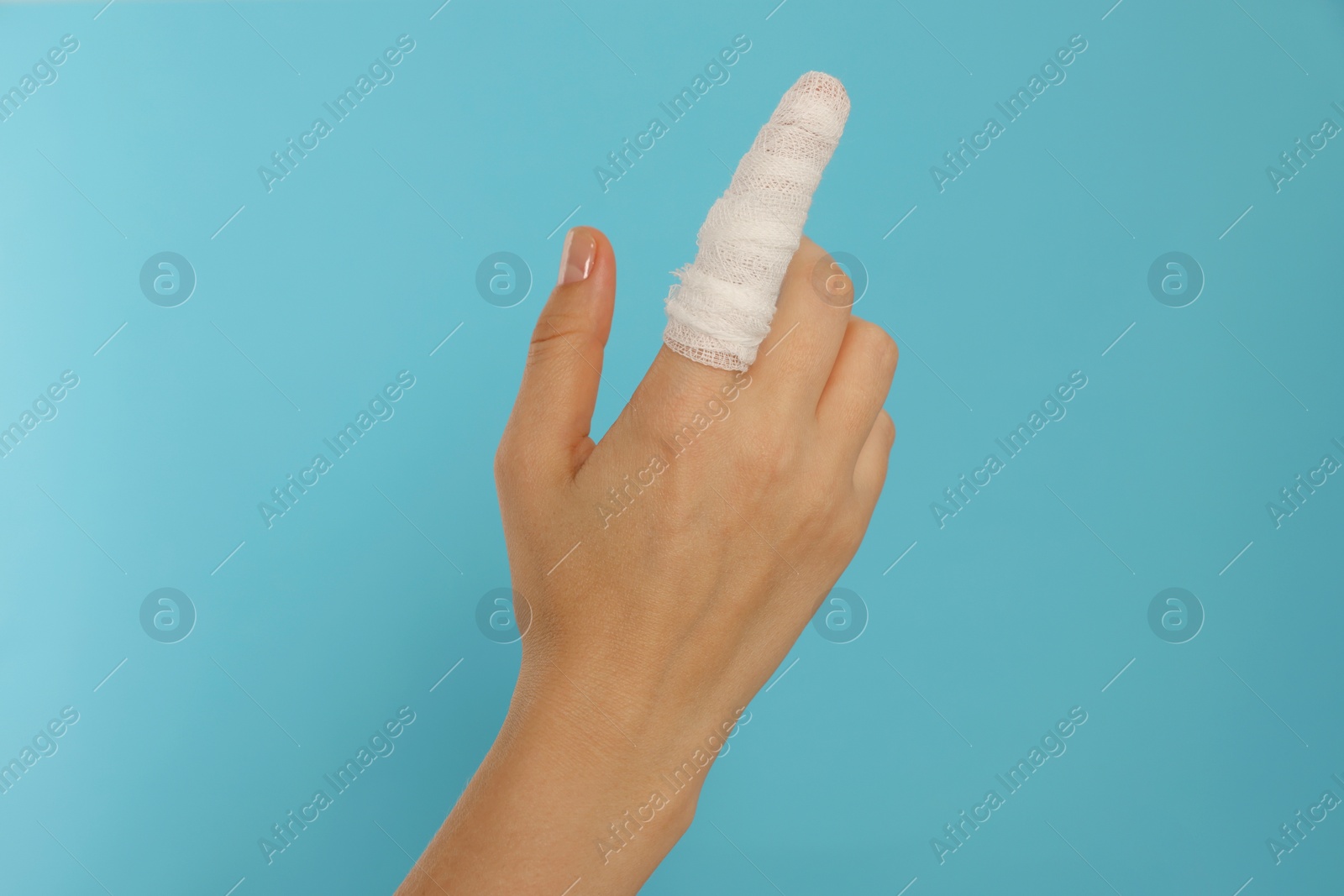 Photo of Woman with finger wrapped in medical bandage on on light blue background, closeup