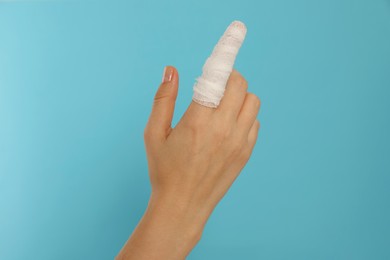 Photo of Woman with finger wrapped in medical bandage on on light blue background, closeup