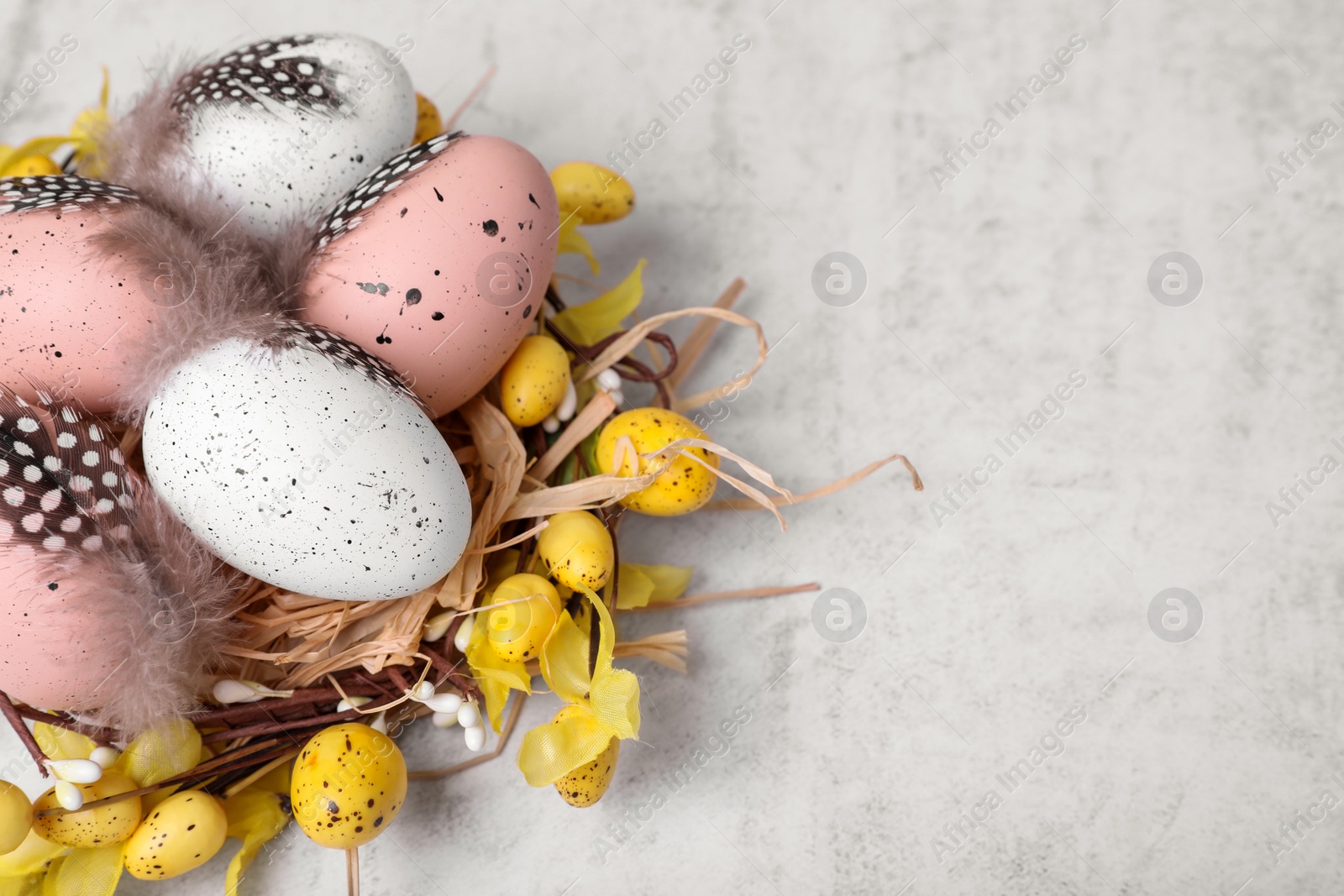 Photo of Decorative nest with many painted Easter eggs on light textured background, closeup. Space for text