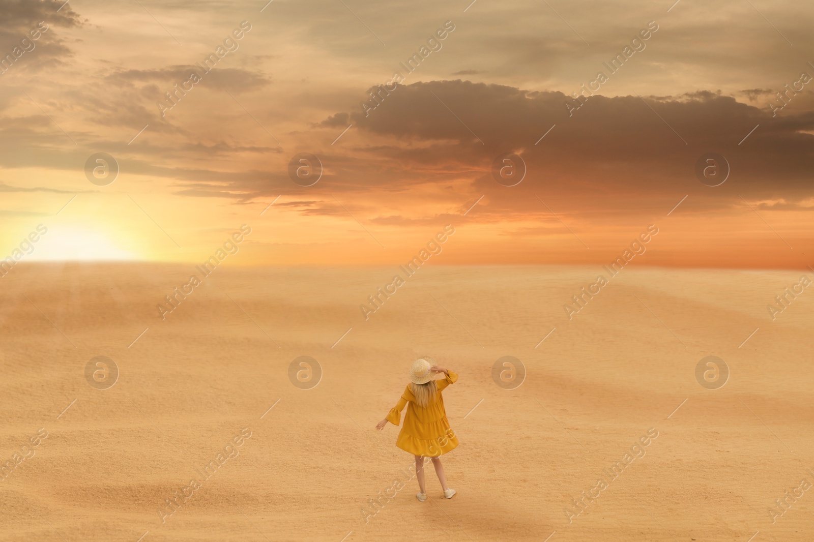 Image of Woman in sandy desert at sunset, back view