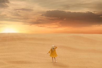 Image of Woman in sandy desert at sunset, back view