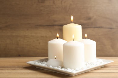 Photo of Plate with burning candles on wooden table. Space for text