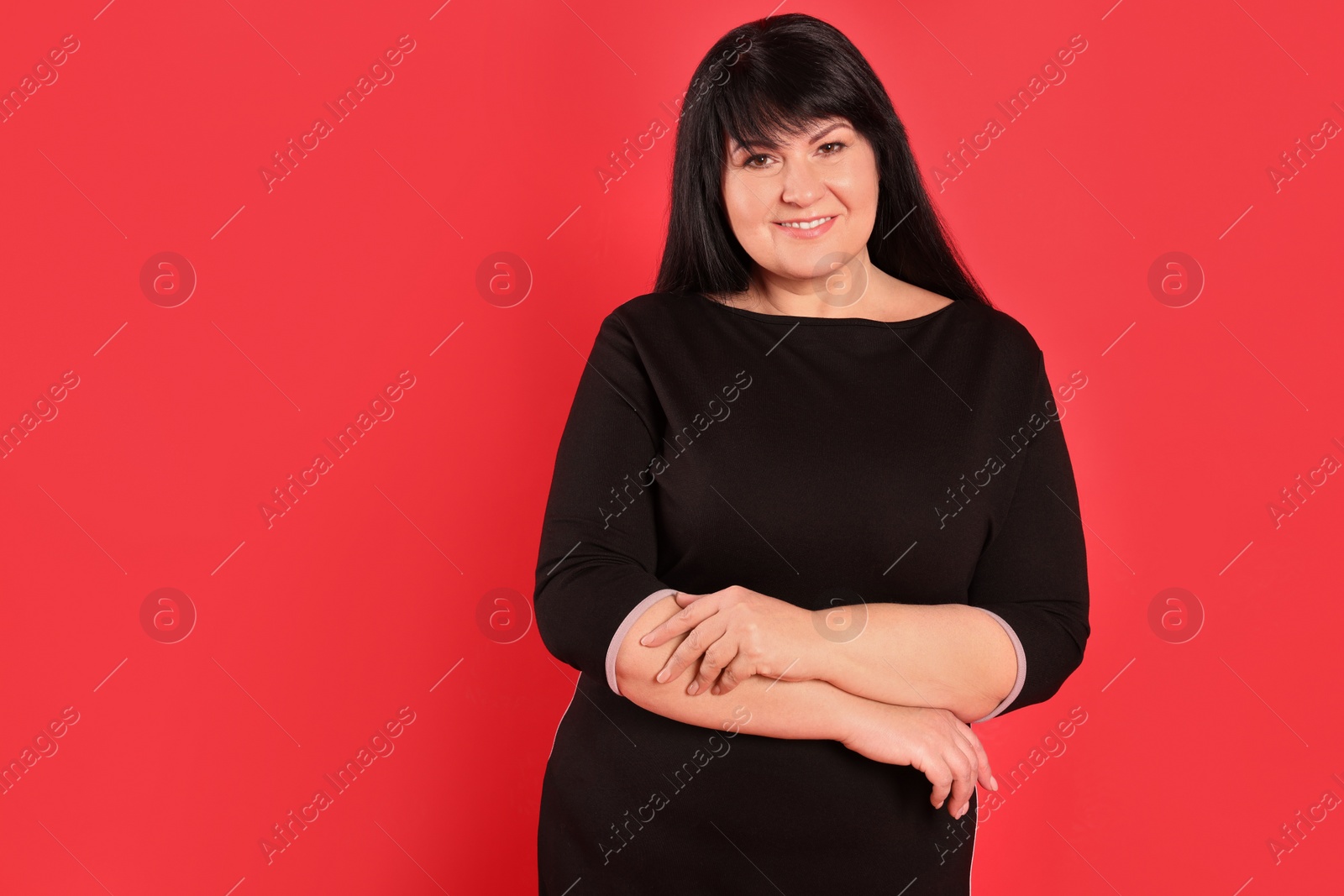 Photo of Beautiful overweight mature woman with charming smile on red background. Space for text