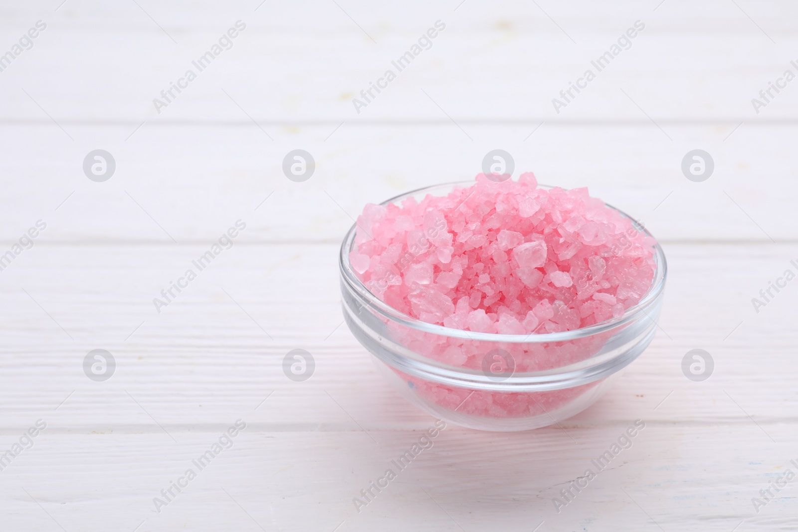 Photo of Bowl with pink sea salt on white wooden table. Space for text