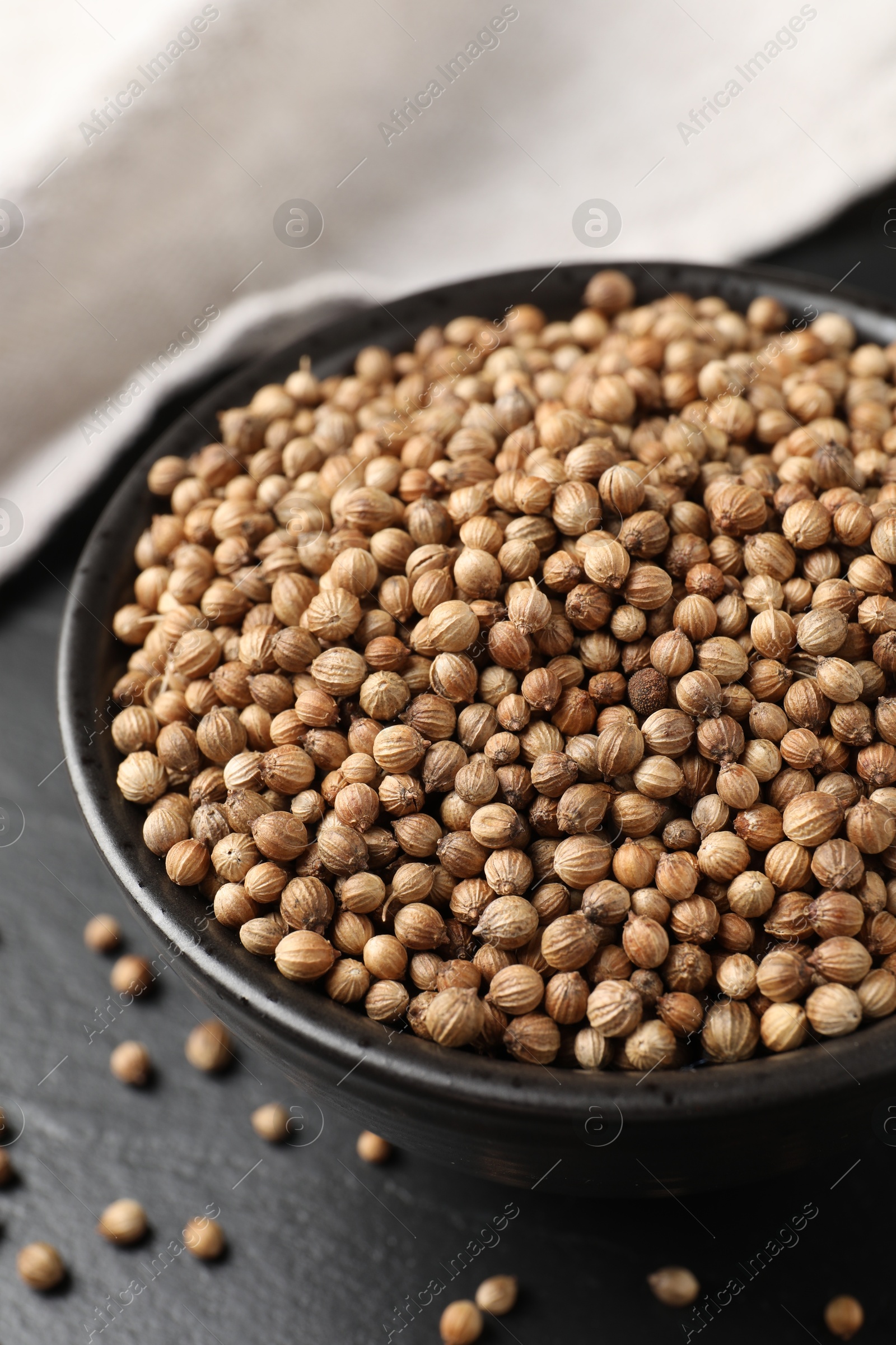 Photo of Dried coriander seeds in bowl on dark gray table, closeup