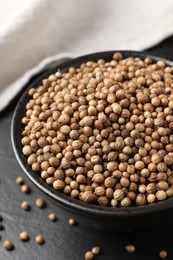 Dried coriander seeds in bowl on dark gray table, closeup