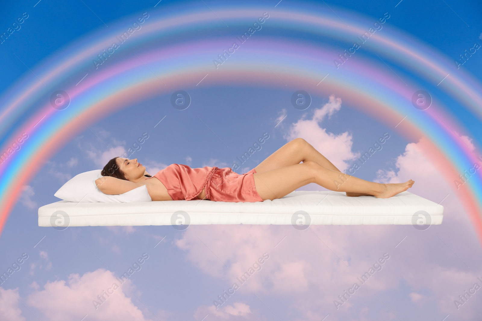 Image of Sweet dreams. Young woman lying on mattress in blue sky with bright rainbow