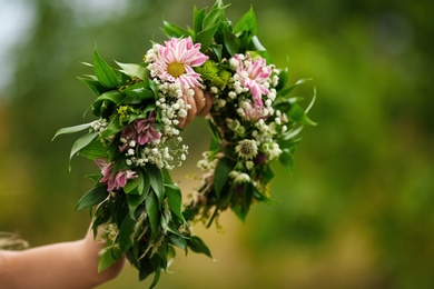 Cute little girl holding wreath made of beautiful flowers outdoors, closeup