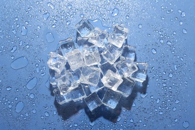 Photo of Pile of melting ice cubes and water drops on blue background, top view