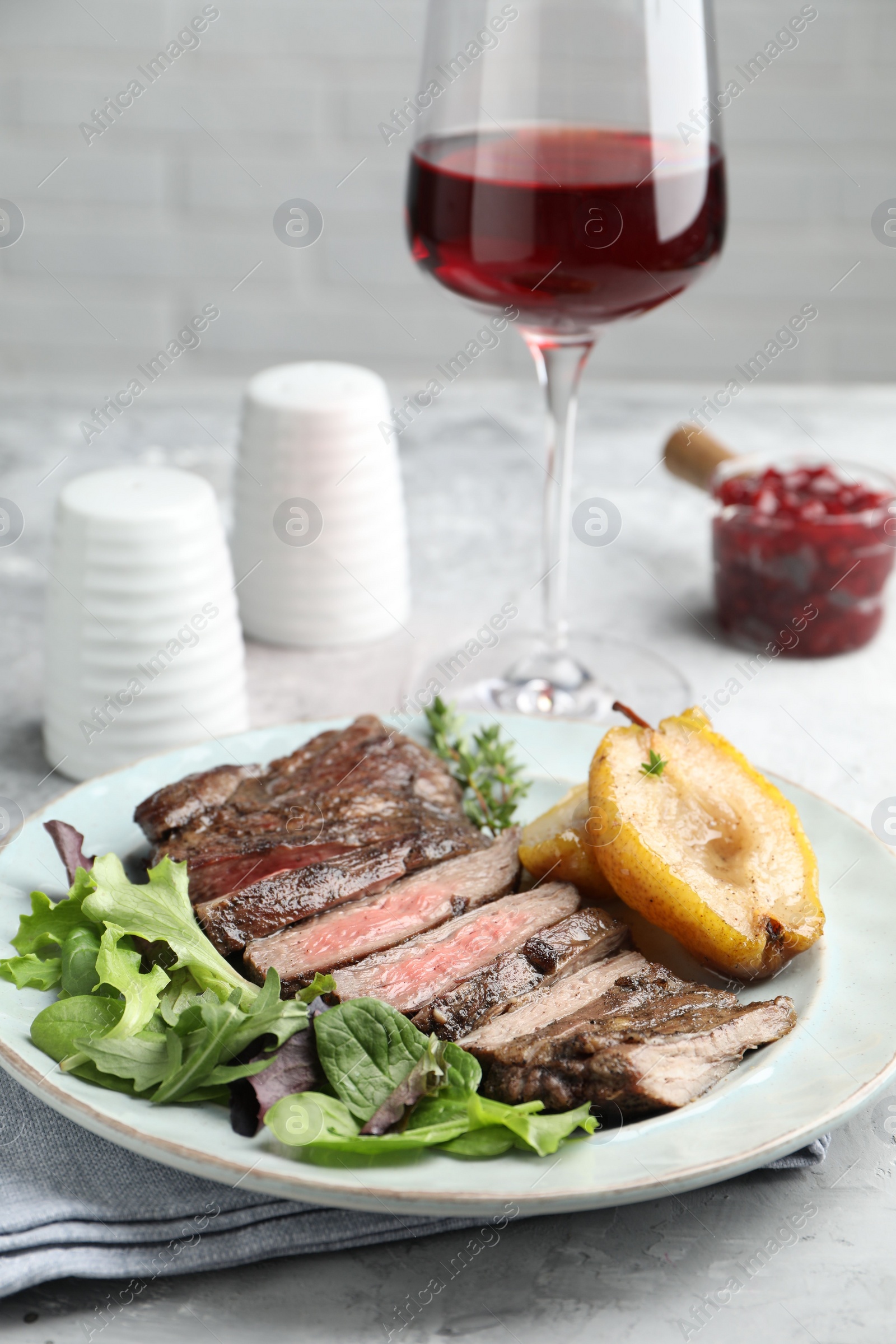 Photo of Delicious roasted beef meat, caramelized pear and greens served on light table