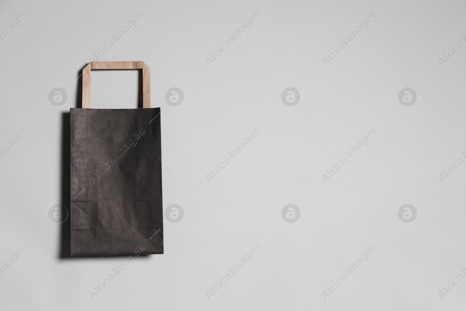Photo of One black paper shopping bag on grey background, top view. Space for text
