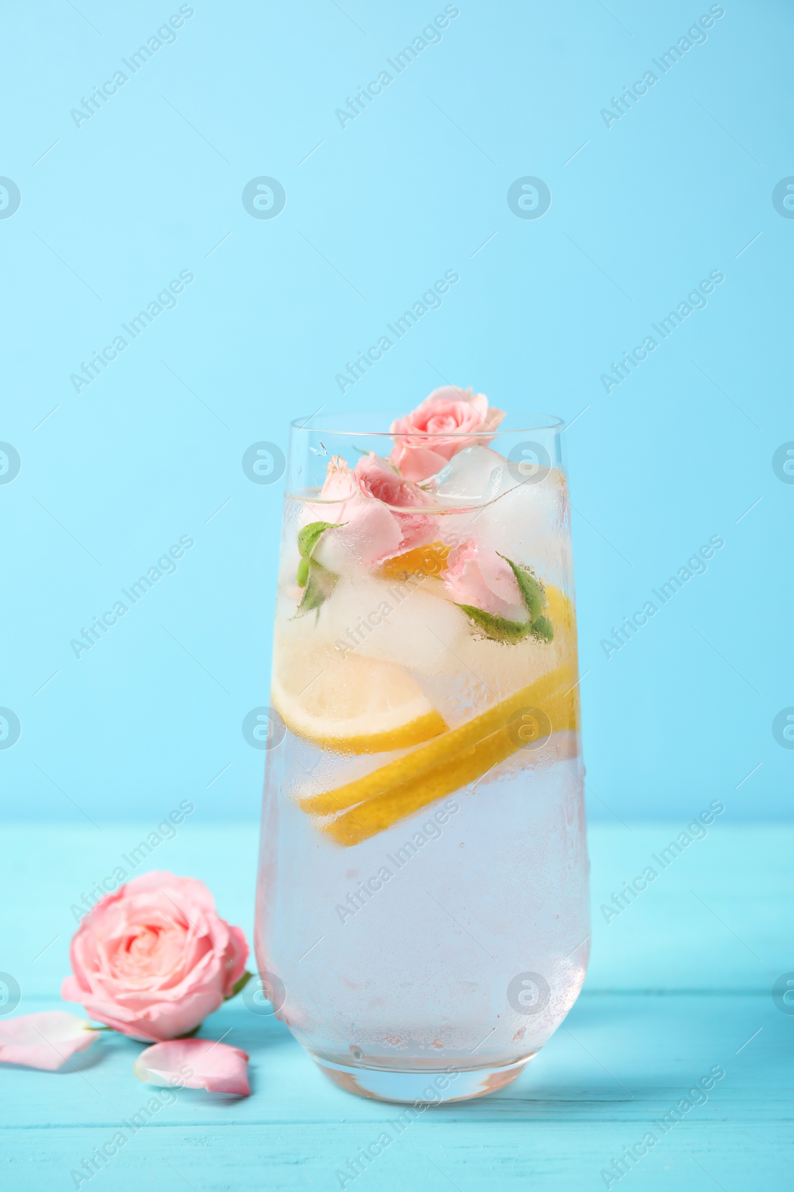 Photo of Tasty refreshing lemon drink with roses on wooden table against light blue background