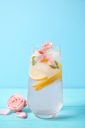 Photo of Tasty refreshing lemon drink with roses on wooden table against light blue background