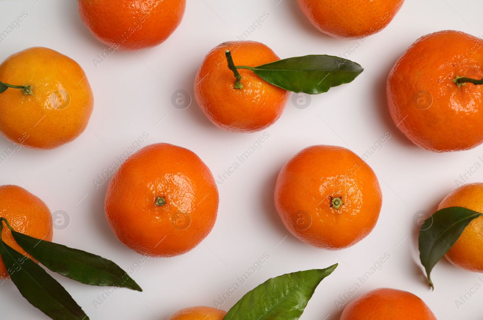 Photo of Delicious tangerines and green leaves on white background, flat lay