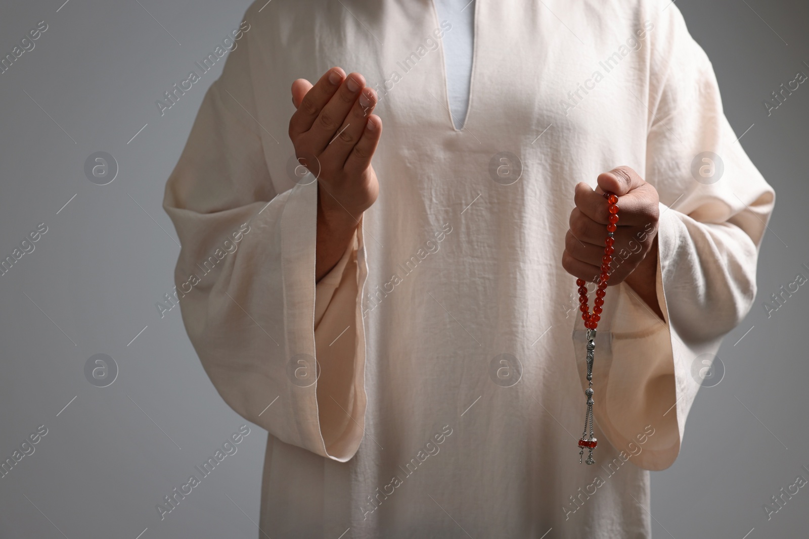 Photo of Muslim man with misbaha praying on light grey background, closeup