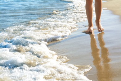 Woman walking on sandy beach near sea, closeup. Space for text