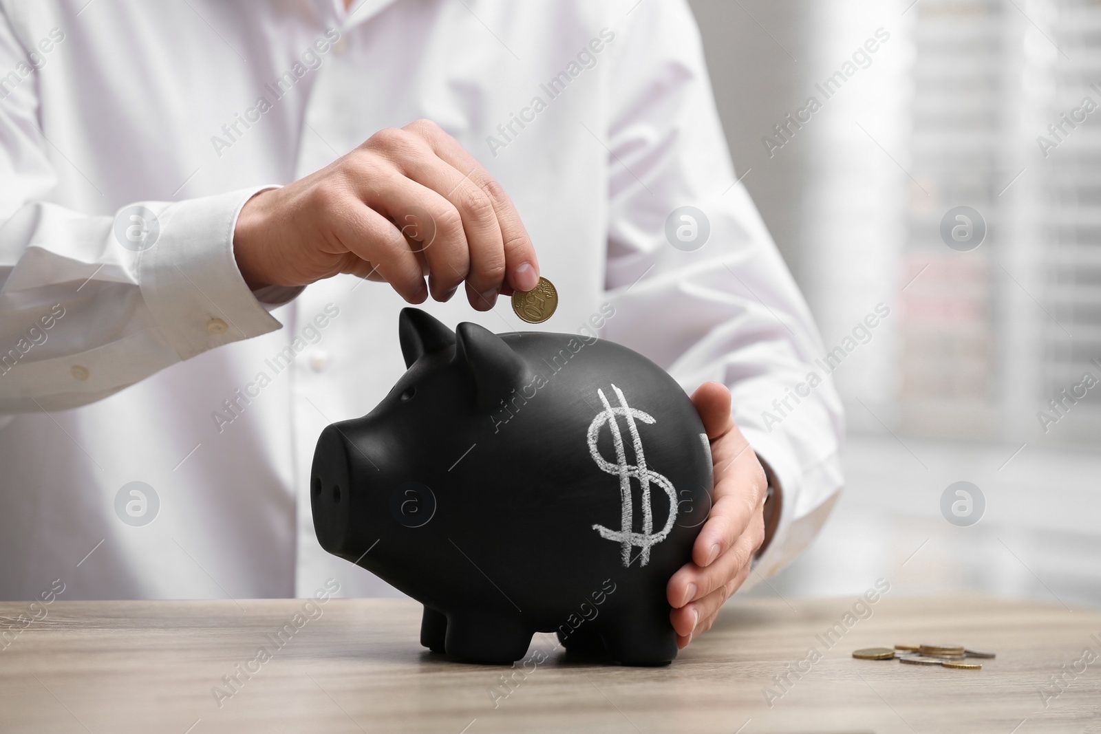 Photo of Man putting coin into piggy bank with dollar sign at wooden table, closeup