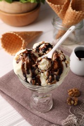 Glass dessert bowl of tasty ice cream with chocolate topping and nuts served on white table