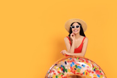 Happy young woman with beautiful suntan, hat, sunglasses and inflatable ring against orange background, space for text
