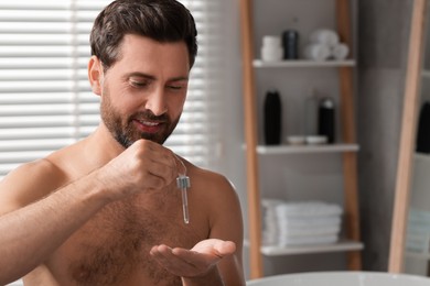 Photo of Smiling man dropping cosmetic serum onto his hand in bathroom. Space for text