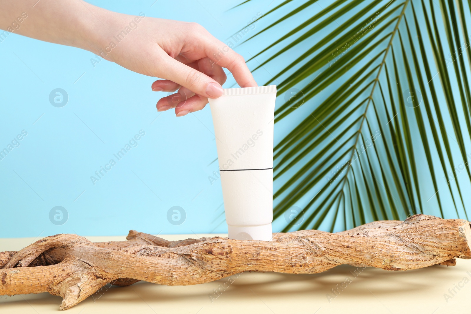 Photo of Woman with tube of cream and plant against light blue background, closeup