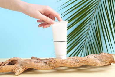 Woman with tube of cream and plant against light blue background, closeup