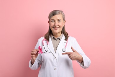 Photo of Mammologist pointing at pink ribbon on color background. Breast cancer awareness