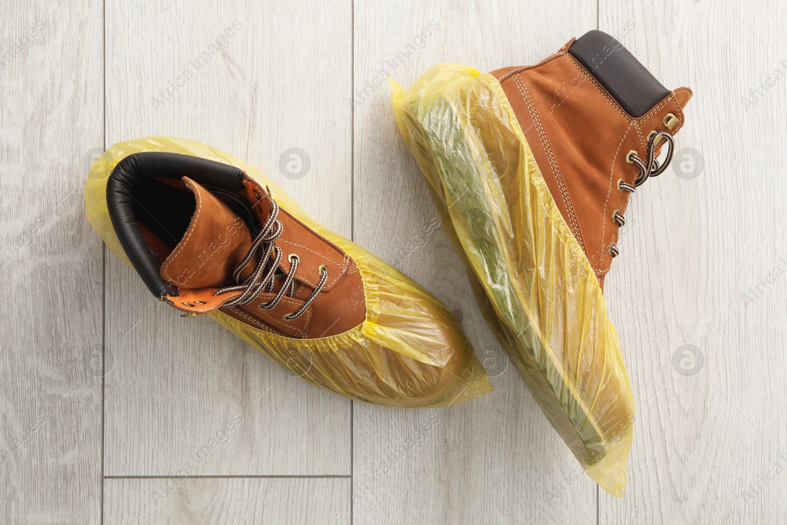 Photo of Men`s boots in yellow shoe covers on light wooden floor, top view