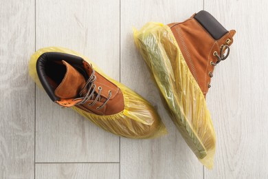 Men`s boots in yellow shoe covers on light wooden floor, top view