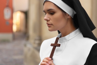Photo of Young nun with Christian cross on city street, closeup. Space for text